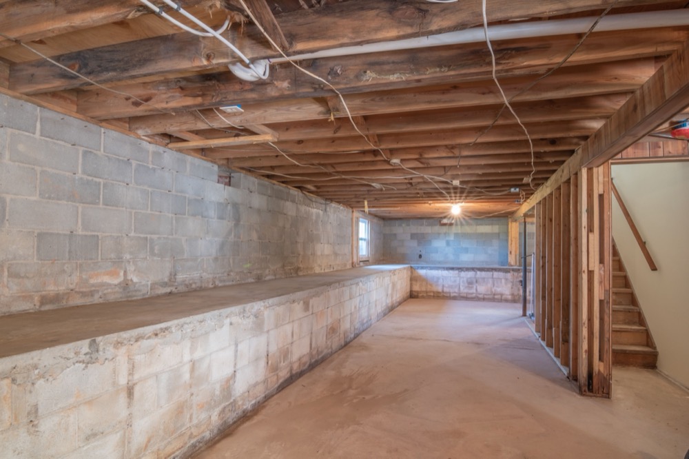 An unfinished basement showing a concrete block foundation wall and wood floor joists